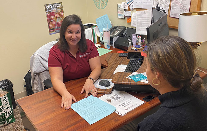 An advisors sits behind a desk across from a student. They are looking at an advising worksheet together. 