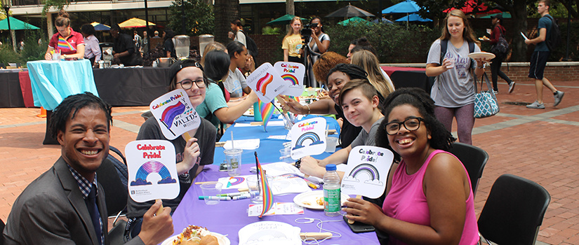 Students holding signs at  BBQueer event at Russell House patio. 