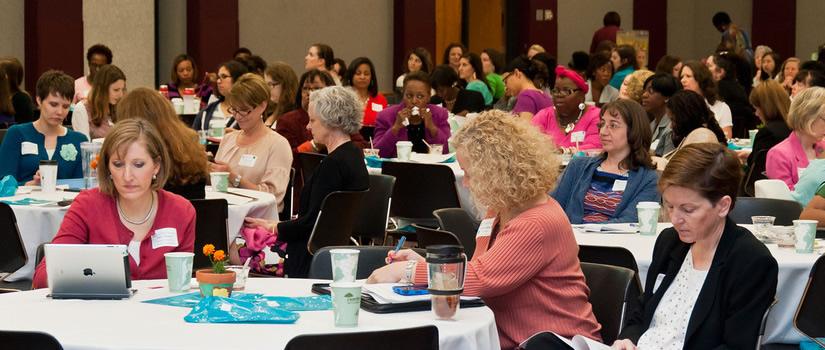 Women sit at round tables between events during a large conference