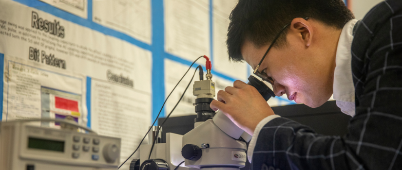 a photo of a student researcher looking through a microscope
