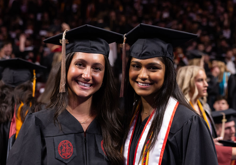 Students in regalia pose for a camera while surrounded by other graduates. 