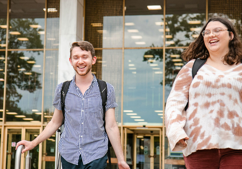 Two students walking down the steps in front of the library. 