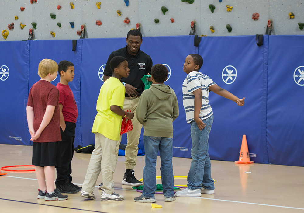 elementary students interacting with a student teacher in a gymnasium