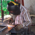  A figure wears a black welding helmet and holds welding equipment while sparks fly. Photo by John Doering-White.