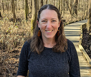 a woman with dark hair and a black heathered long sleeve shirt smiling on a trail