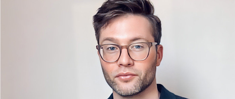 man with dark glasses on in front of a off white back drop