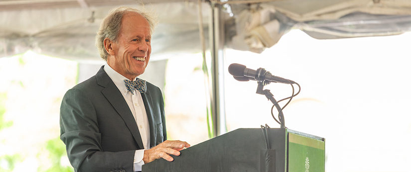 Peter McCausland smiles while delivering a speech at the podium under a white event tent at the University of South Carolina.