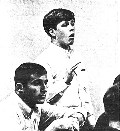 A black-and-white archival photo of a young Peter McCausland speaking passionately in a classroom setting during his time as a USC student.