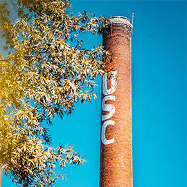 The smokestack with the letters USC on it framed by tree limbs in front of a blue sky.