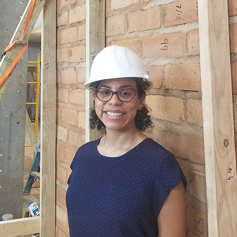 a woman standing in front of a wall wearing a hard hat