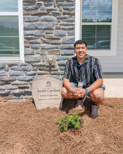 Juan Alvarado posing next to the USC College of Education "Educators in Residence" stone plaque outside his home.