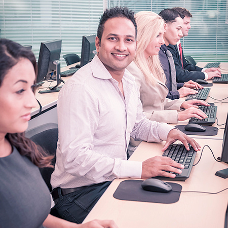 A group of people sitting at computer stations, one person smiles at the camera.