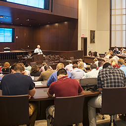 wideshot of auditorium filled with students in foreground and professor at podium in background.