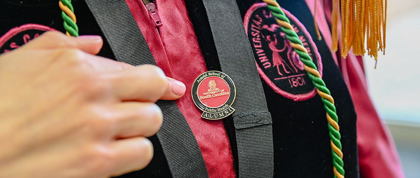 Alumni pointing to official UofSc alumni pen on graduation gown