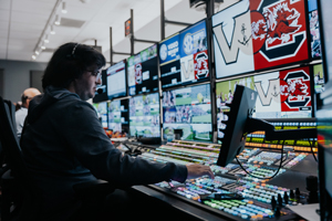woman wearing a headset sits at a bank of TVs
