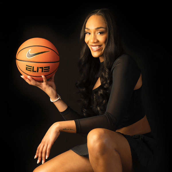Aja Wilson smiles for the camera with a basketball on a black background.