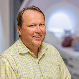 Julius Fridriksson smiles into the camera, while behind him is body scanning machinery