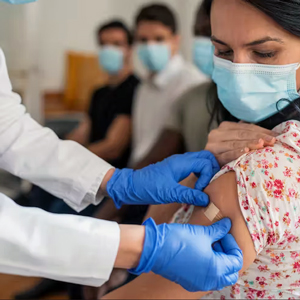 woman watches as a gloved health care worker puts a bandage on her arm 