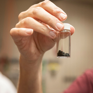 a hand holds a small vial with a dark substance inside