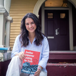 woman sits on a porch and holds a book titled 