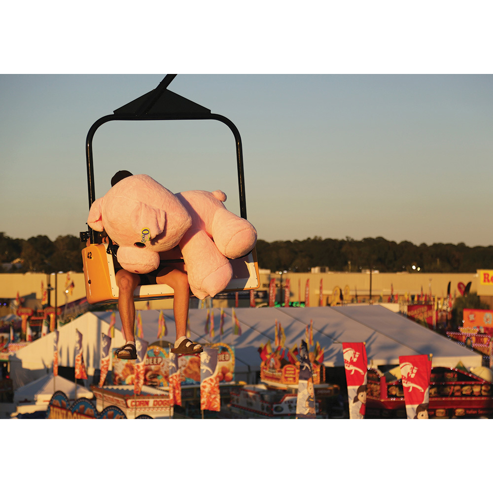 A person on the sky tram at the SC State Fair holding a stuffed bear.
